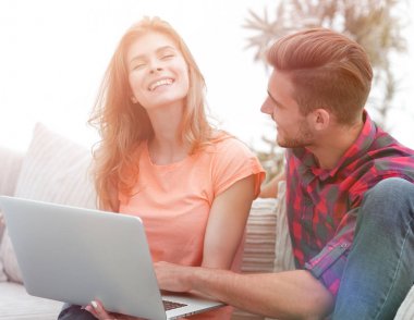 genç bir çift bir dizüstü bilgisayar kullanarak ve evde kanepede otururken gülümseyen