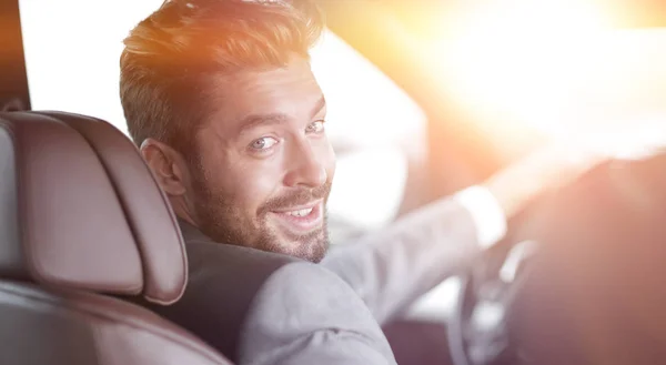 Rückansicht, junger Mann fährt Auto, blickt in Kamera — Stockfoto