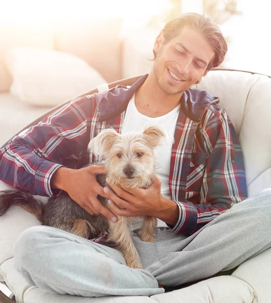 Handsome guy with a dog sitting in a large armchair. — Stock Photo, Image