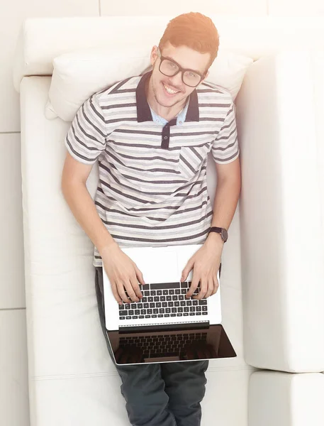 Modern man works on a laptop sitting on the couch — Stock Photo, Image