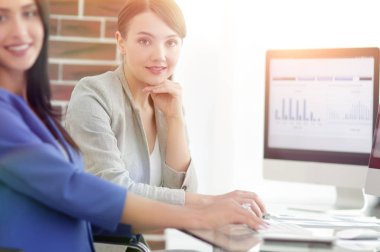 Kameraya bakarak ve oturma işyerinde gülümseyen genç kadın