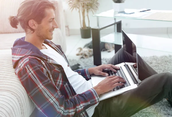 Moderne man met een laptop die zittend op de vloer in de buurt van de Bank — Stockfoto