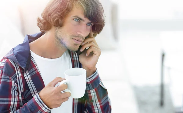 Hermoso chico con una taza se sienta delante de un ordenador portátil . — Foto de Stock