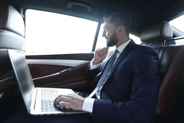 Empresario escribiendo texto en el ordenador portátil mientras está sentado en el coche —  Fotos de Stock