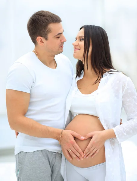 Marido e mulher grávida com as mãos dobradas na forma de um coração em sua barriga — Fotografia de Stock