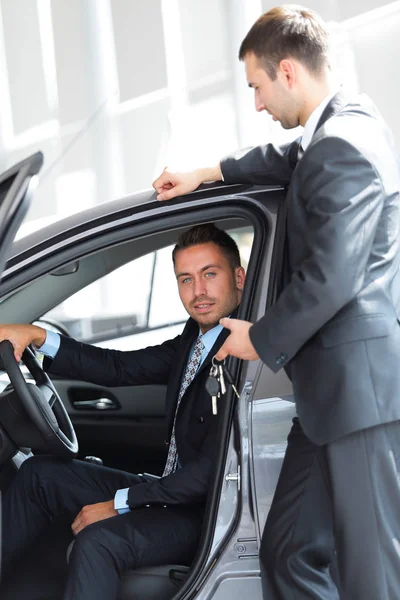 Úspěšný podnikatel, přijímání klíče k autu od prodávajícího v showroomu — Stock fotografie