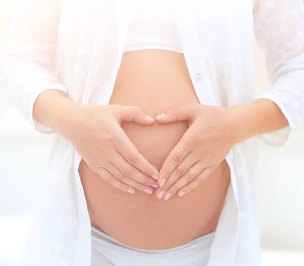 Pregnant woman holding hands in heart shape on her belly. — Stock Photo, Image