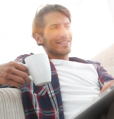 dizüstü bilgisayar yakınındaki inci katta oturan bir fincan holding ile genç adam