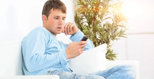 Image of a young man sitting on the couch and using a phone — Stock Photo, Image