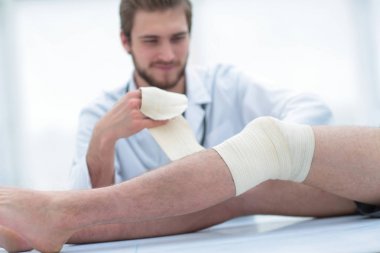 Doktor hastanın bacak üzerinde bir yara sarmak