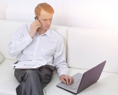 laptop ile çalışan ve bir cep telefonuyla konuşan işadamı