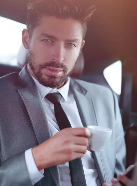 Uomo d'affari che beve caffè sul sedile posteriore di una macchina — Foto Stock