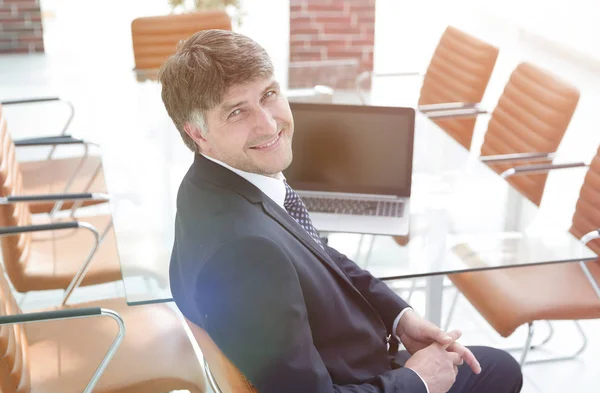 Χαμογελώντας manager που κάθεται στο γραφείο εργασίας σε αίθουσα συνεδριάσεων. — Φωτογραφία Αρχείου