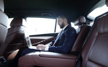 bir arabanın arka koltuğunda bir dizüstü bilgisayar kullanarak iş adamı