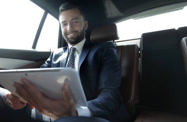 bir arabanın arka koltuğunda çalışma ve bir tablet kullanarak iş adamı