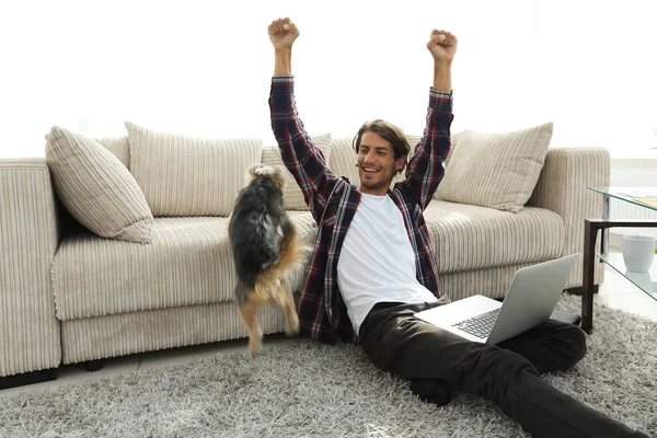 Jovem feliz exulta com seu cão sentado na sala de estar — Fotografia de Stock