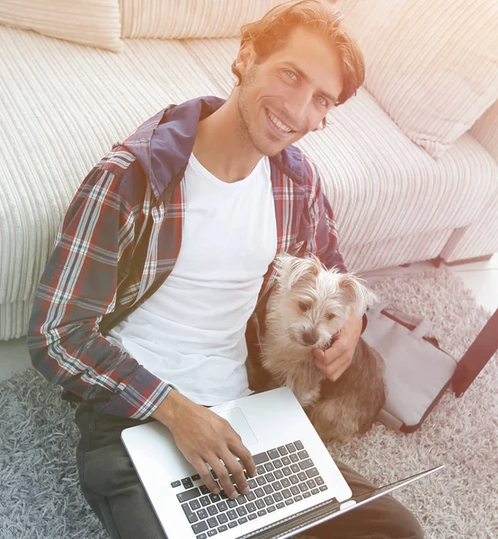 Schöner Kerl mit Laptop umarmt seinen Hund und sitzt in der Nähe der co — Stockfoto