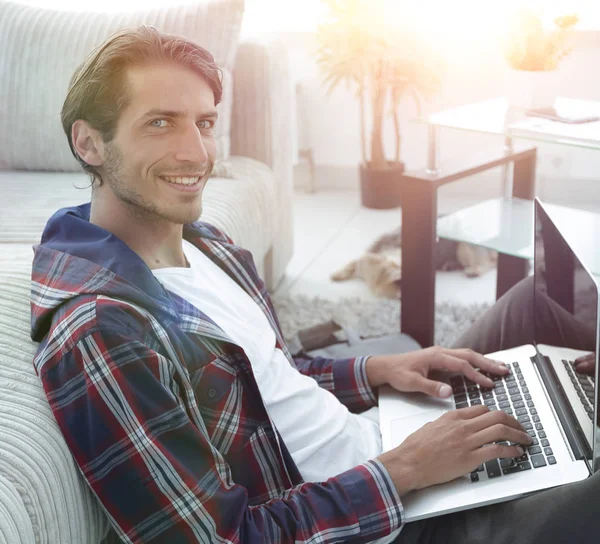 Glimlachende man met een laptop die zittend op de vloer in de buurt van de Bank — Stockfoto