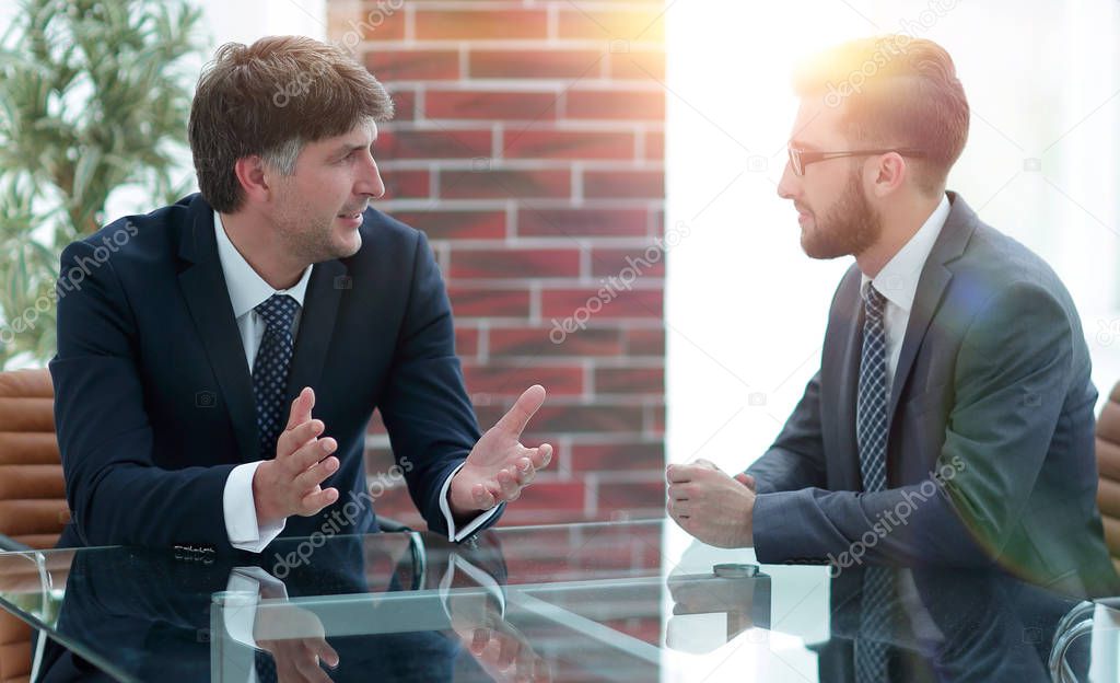 Two businessmen discussing tasks sitting at office table.