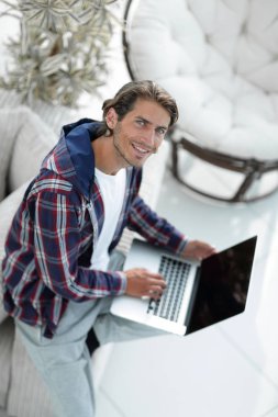 dizüstü bilgisayarda çalışan ve kameraya bakarak bir genç adam. Yukarıdan görüntülemek