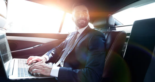 Hombre de negocios con portátil sentado en el asiento trasero de un coche — Foto de Stock
