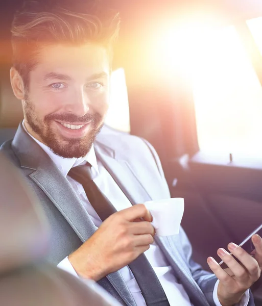 Uomo d'affari che beve caffè in auto con il telefono in mano — Foto Stock