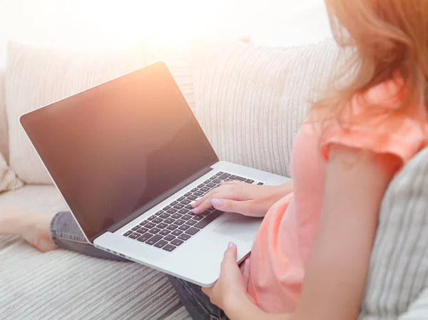 Ung kvinna som arbetar med laptop sitter på soffa — Stockfoto