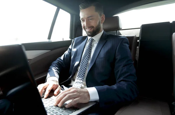 Uomo d'affari seduto sul sedile posteriore di una macchina, utilizzando il suo computer portatile — Foto Stock