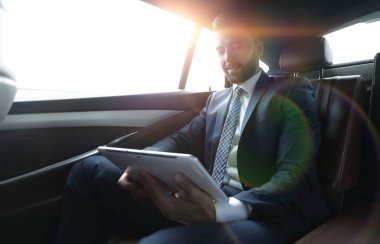 bir arabanın arka koltuğunda çalışma ve bir tablet kullanarak iş adamı