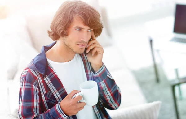 Schöner Kerl mit einer Tasse sitzt vor einem Laptop. — Stockfoto