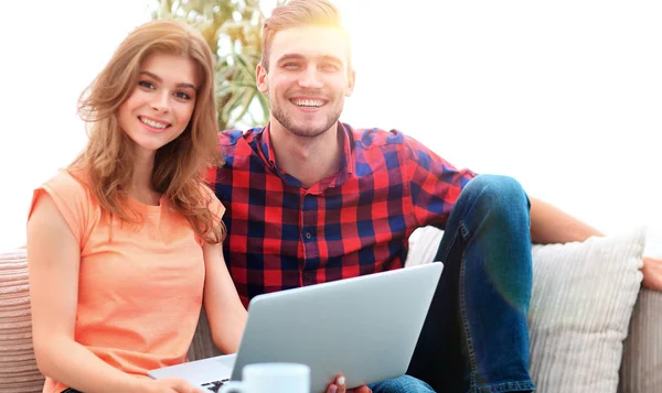 Young couple of students uses a laptop sitting on sofa — Stock Photo, Image