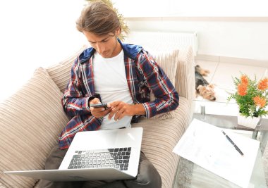 dizüstü bilgisayar ve akıllı telefon oturma odasında ciddi genç adam.