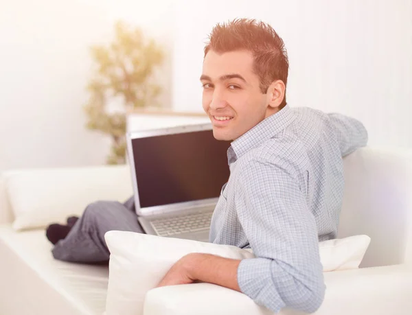 Handsome man is using a laptop, looking at camera and smiling — Stock Photo, Image