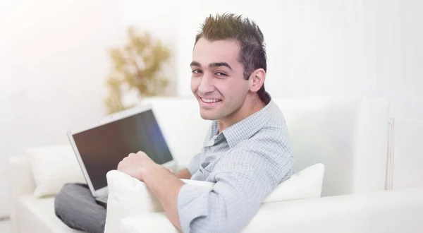 Schöner Mann benutzt einen Laptop, schaut in die Kamera und lächelt — Stockfoto