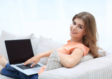 güzel genç kadın kanepede oturan ve kameraya bakarak dizüstü bilgisayar ile çalışma.