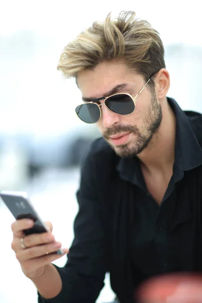 Ein stylischer bärtiger Mann sitzt und benutzt ein Smartphone. — Stockfoto