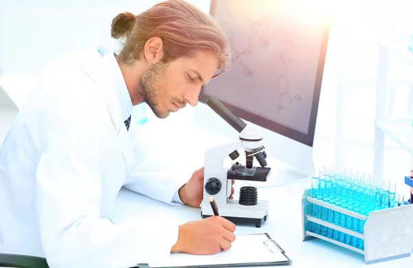 Trabajador de laboratorio sentado a la mesa con microscopio —  Fotos de Stock