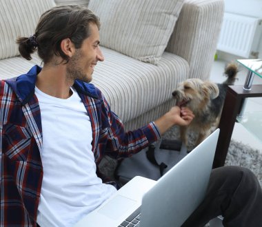 hayvanını okşayarak ve dizüstü bilgisayarda çalışan şık genç adam