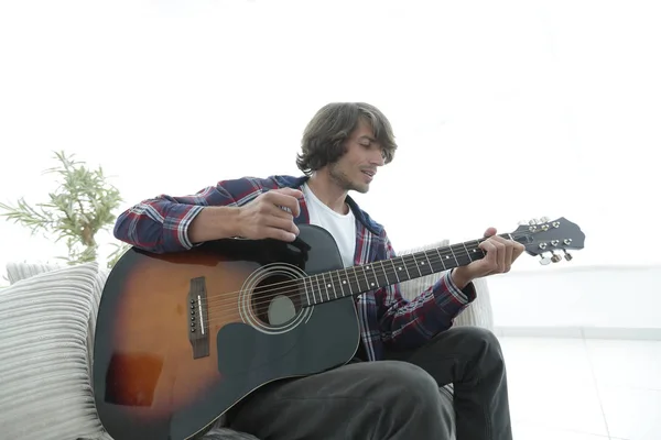 Cara canta uma música e toca guitarra sentado no sofá . — Fotografia de Stock