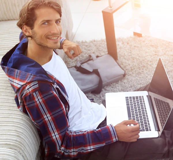 Zakelijke man met laptop zitting op tapijt in de woonkamer. — Stockfoto