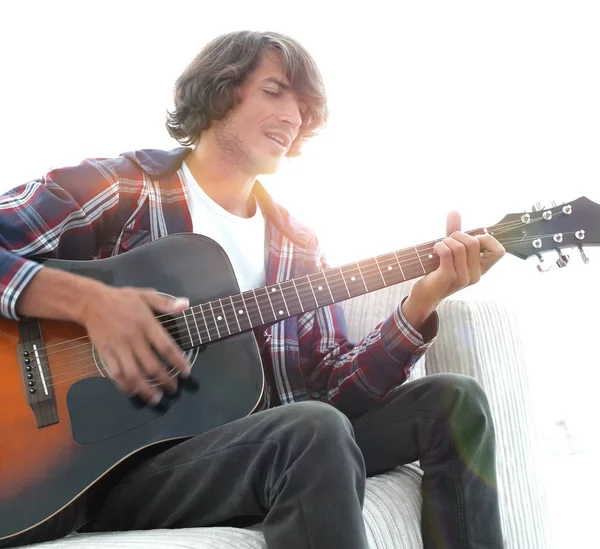 Cara canta uma música e toca guitarra sentado no sofá . — Fotografia de Stock