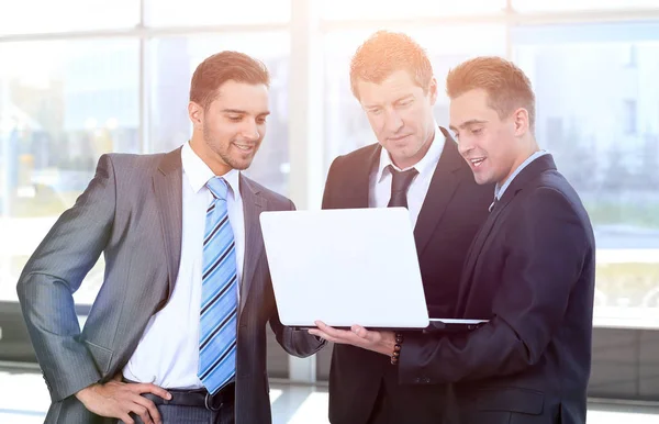 Business colleagues looking at a laptop, standing in the lobby o — Stock Photo, Image
