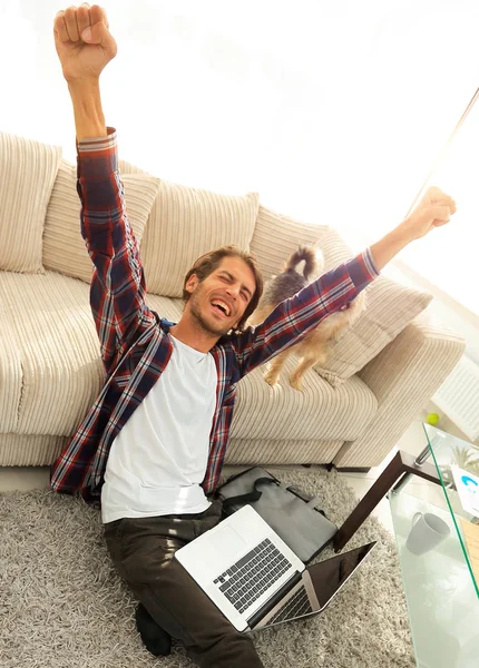 Cara feliz com laptop jubilante na espaçosa sala de estar . — Fotografia de Stock