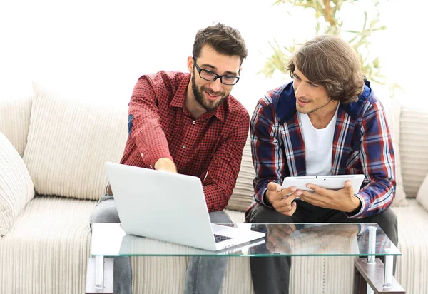 Dois jovens trabalhando com laptop e tablet sentado no sofá — Fotografia de Stock