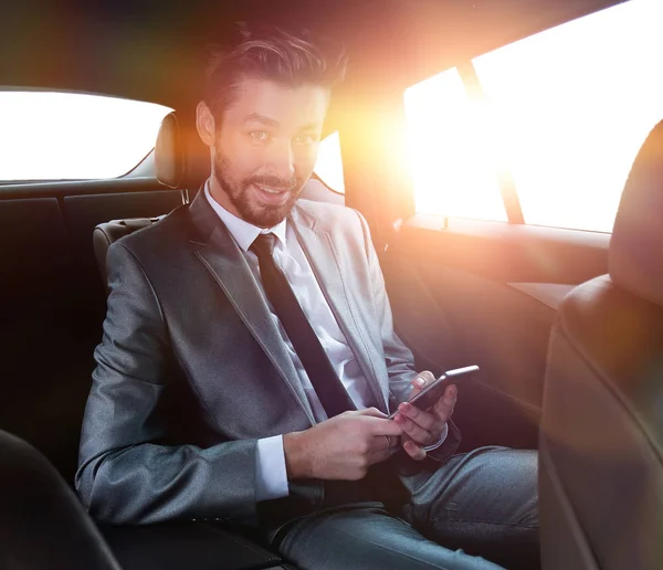 穿着西装的人坐在车上, 在智能手机上阅读信息 — 图库照片