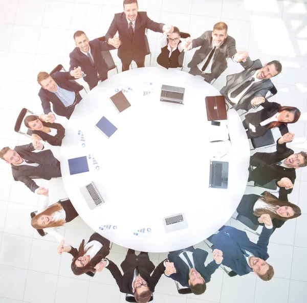 Director y equipo de negocios sentados en la mesa redonda y tomados de la mano . —  Fotos de Stock