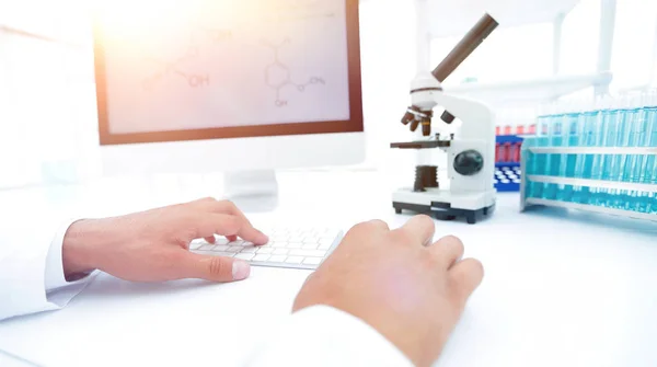 A scientist uses a computer and a microscope — Stock Photo, Image