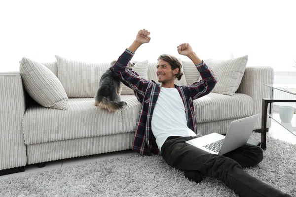 Jovem feliz exulta com seu cão sentado na sala de estar — Fotografia de Stock