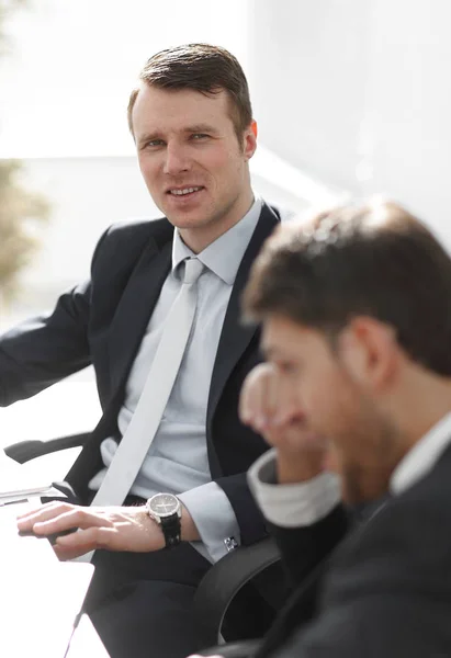 Succesvolle zakenman met zijn collega zitten achter een bureau. — Stockfoto