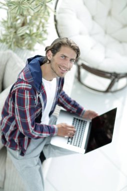 dizüstü bilgisayarda çalışan ve kameraya bakarak bir genç adam. Yukarıdan görüntülemek